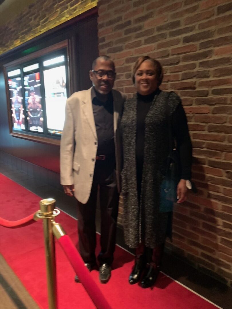 A man and women standing on a red carpet near a wall